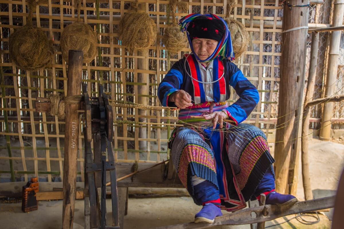 Black Hmong woman weaving traditional fabric in a village