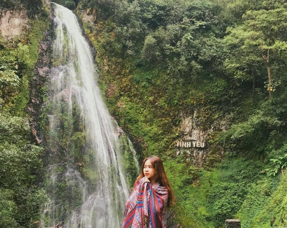 Person taking photos of a waterfall surrounded by greenery